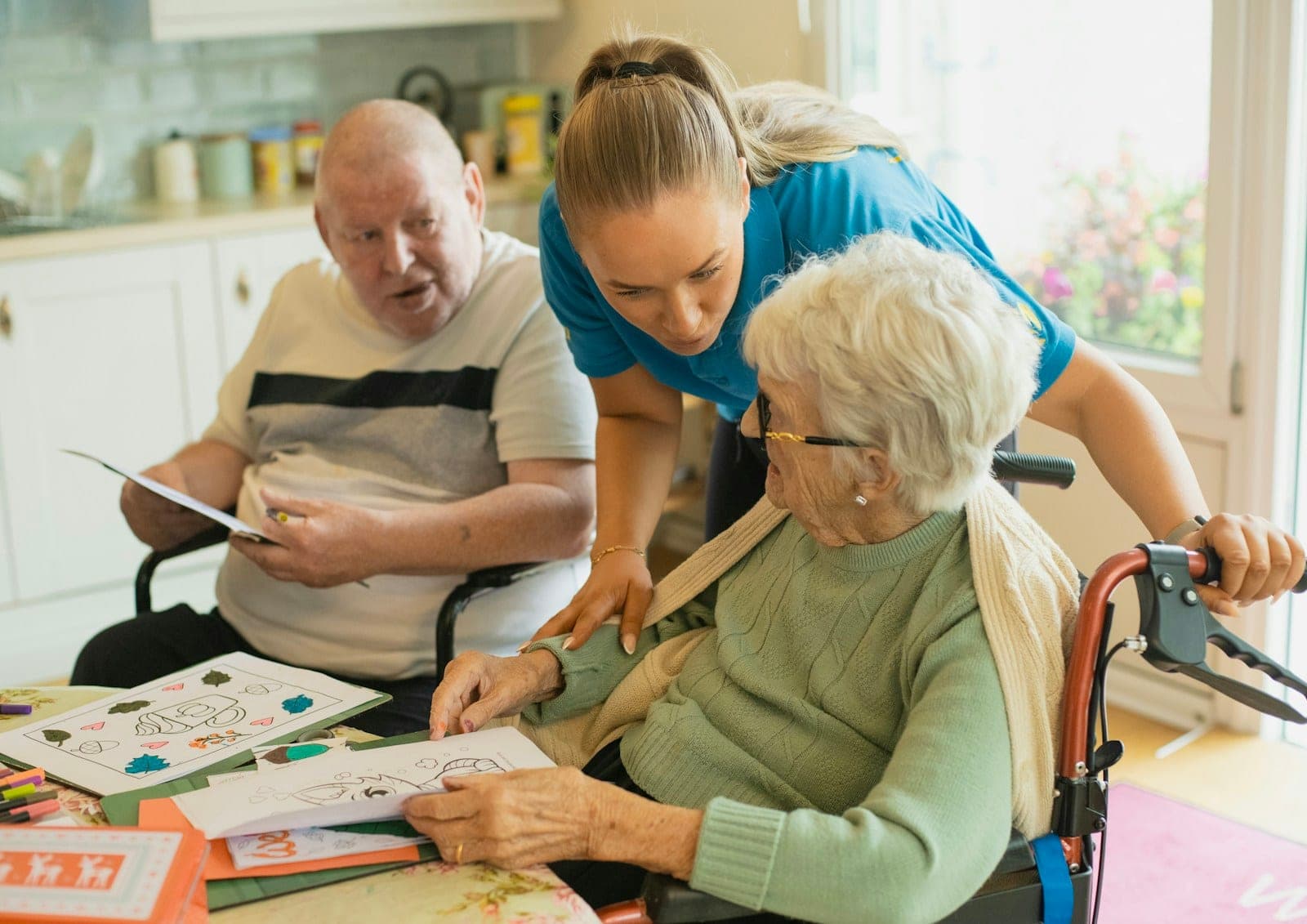 A caregiver helping an older couple with an activity at a table