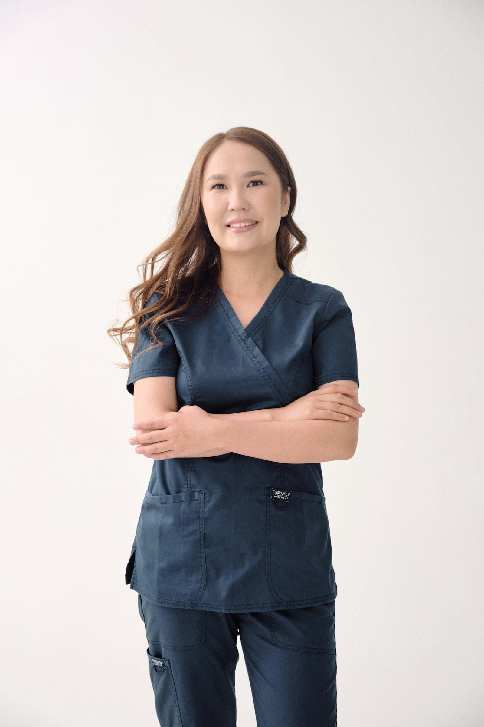 A care professional in scrubs standing against a neutral wall